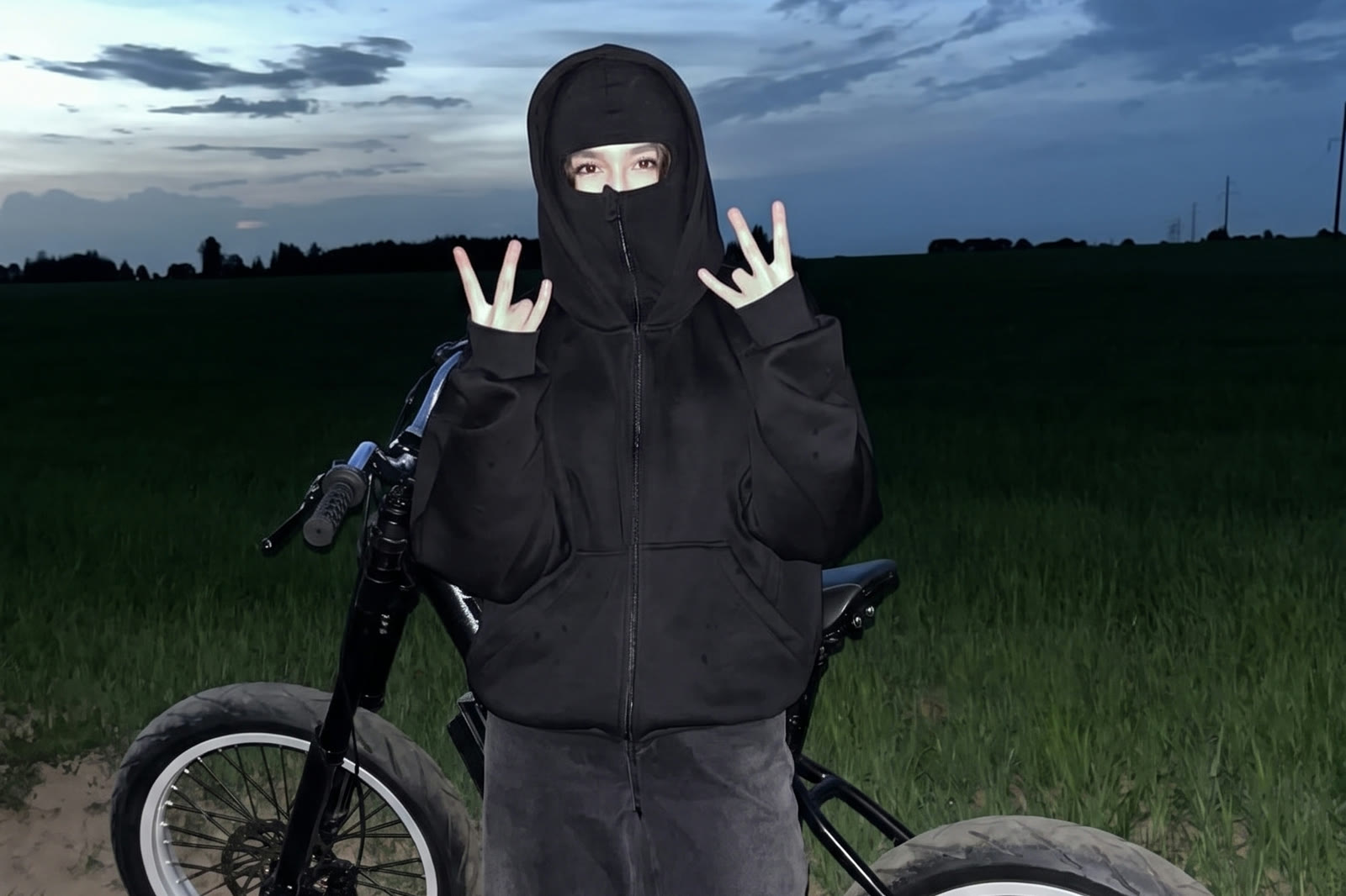 Rider throwing peace signs beside an F1 e-bike at dusk